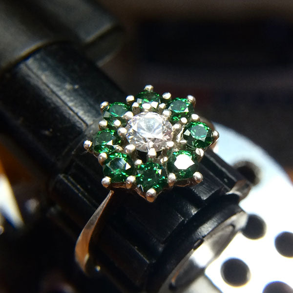 Ring with green gemstones and a diamond on a jewelers bench tool